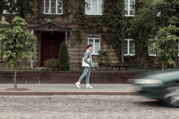 european-fashionable-young-man-stylish-jeans-clothes-sneakers-with-fabric-bag-walks-street-near-road-fashion-urban-guy-travel-city-near-old-building-overgrown-with-leaves