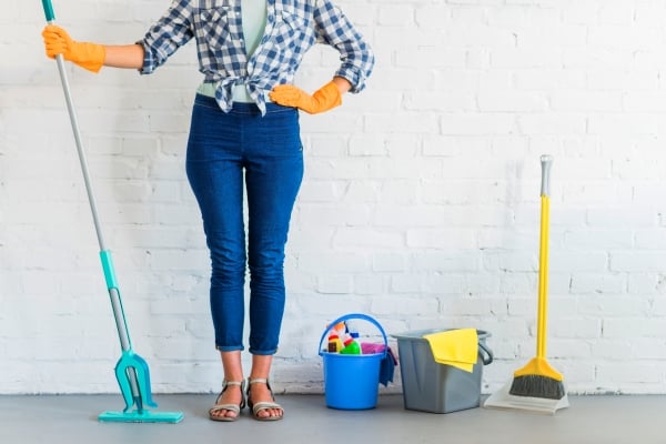 woman-standing-front-brick-wall-with-cleaning-equipments