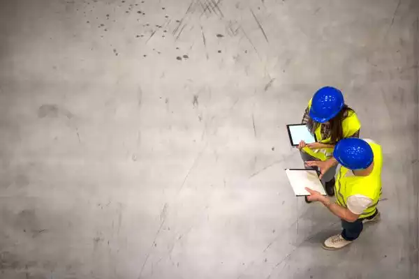 top-view-two-industrial-workers-wearing-hardhats-reflective-jackets-holding-tablet-checklist-gray-concrete-floor-1